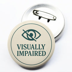 Beige circular badge displaying VISUALLY IMPAIRED with eye icon and pinback