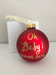 Hand lettered with gold ink Oh Baby Coming 2026 on red ornament